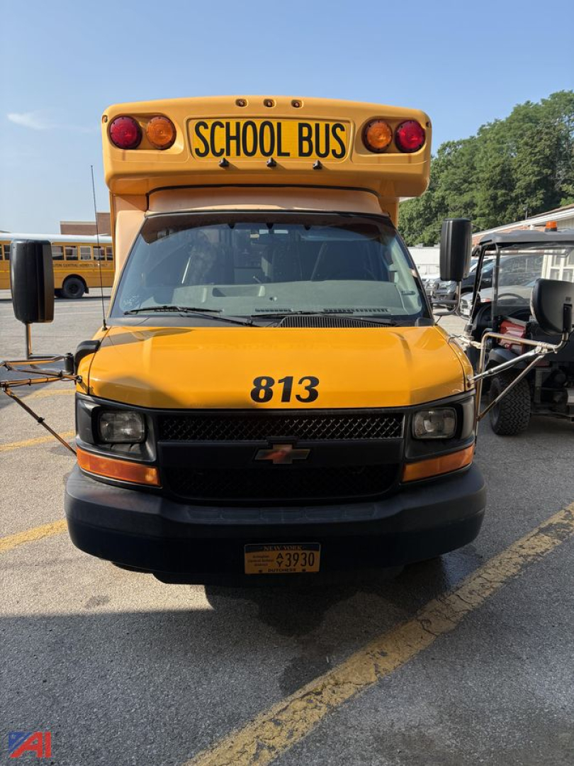 Front of a yellow 2016 Chevrolet Express G3500 mini school bus with number 813 and black grille, school bus sign on top, in a parking lot.
