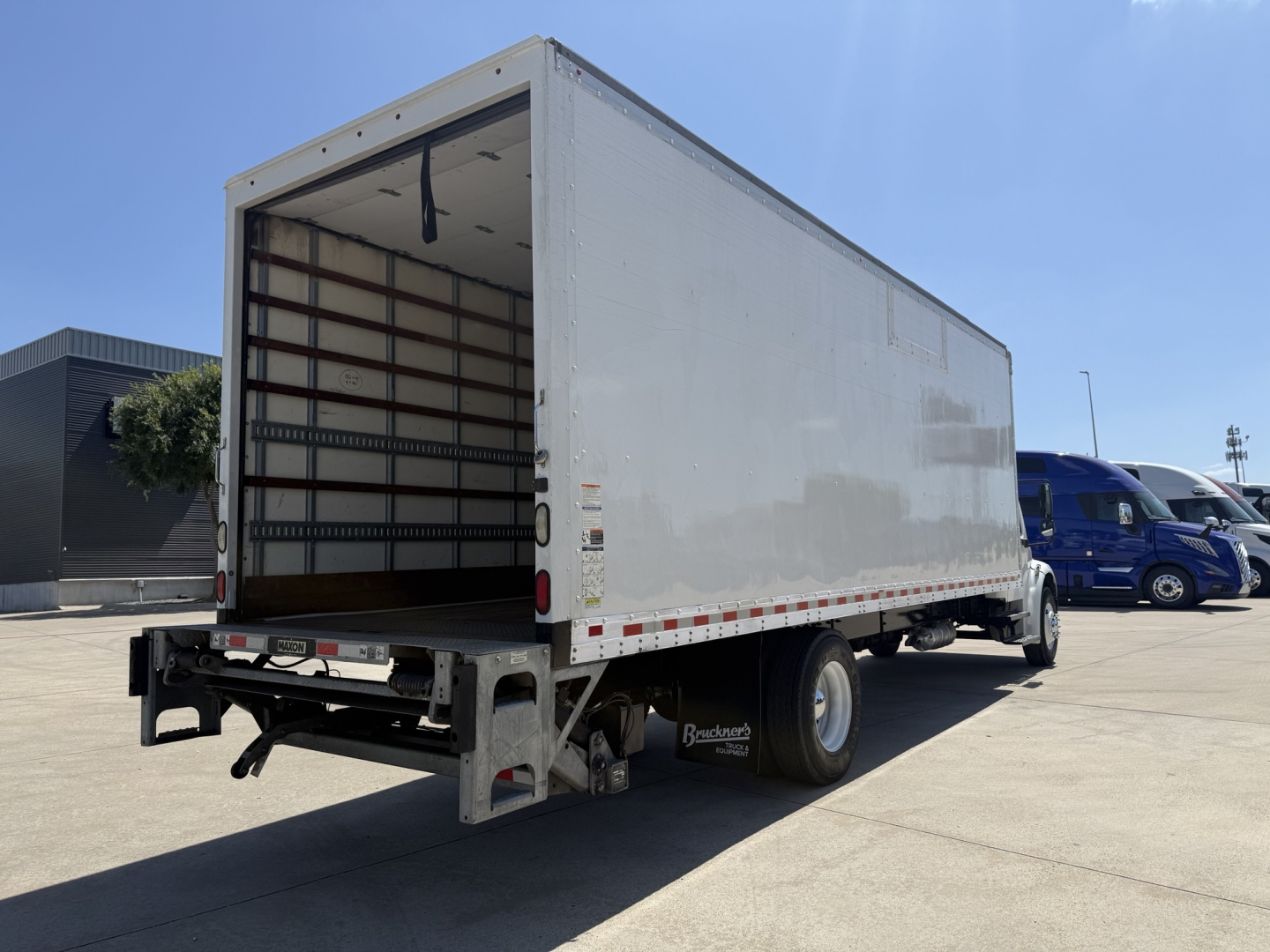 Freightliner M2 box truck cargo area open rear showing empty interior, side profile, rear bumper, and wheel fenders.