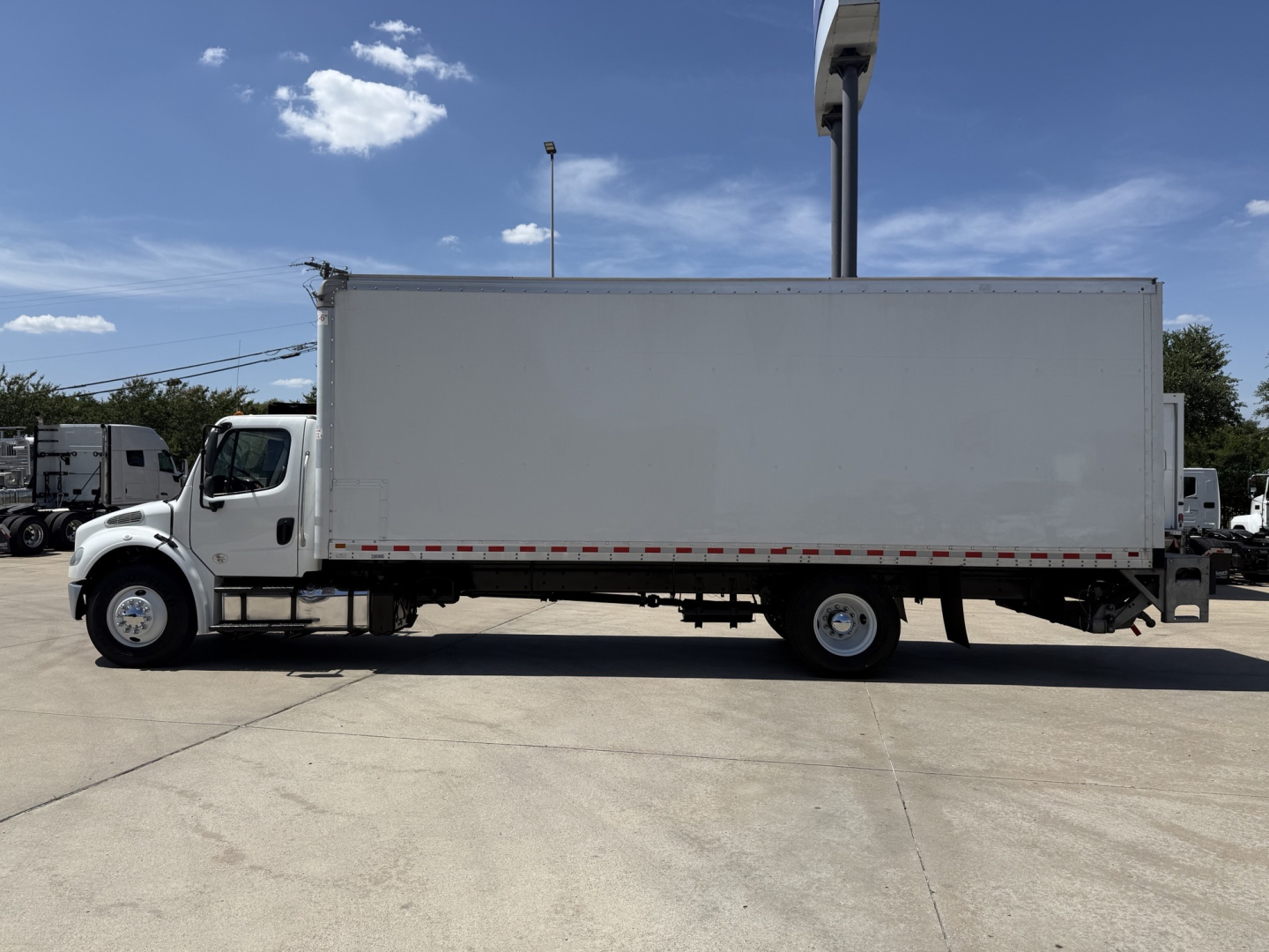 Box truck side view showing a white Freightliner M2 cargo box with cab, long rectangular cargo area, and dual rear axles.
