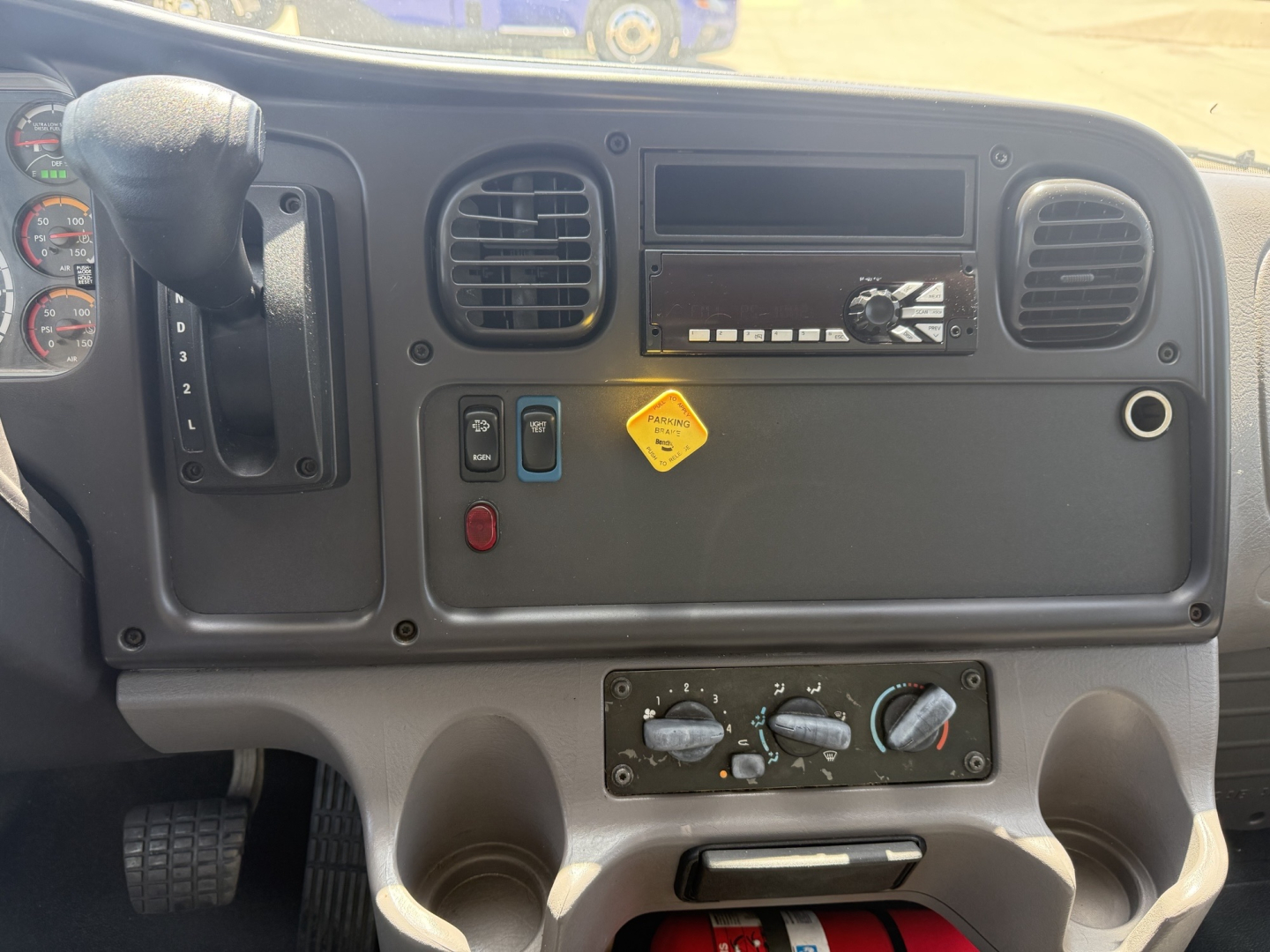 Cabin dashboard of a Freightliner M2 showing steering column, air vents, radio slot, climate controls, and three switches; front panel with hazard and utility indicators.