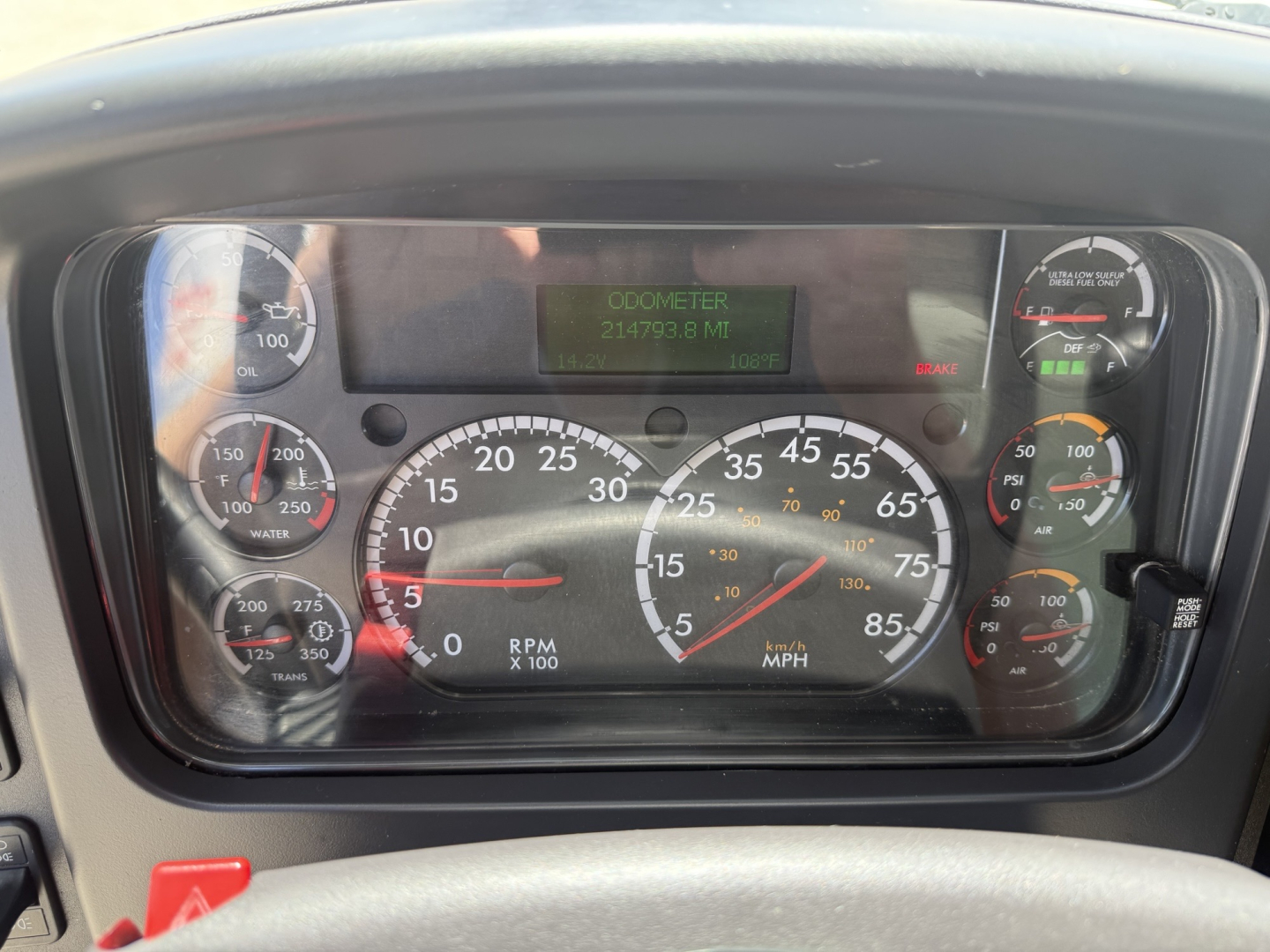 Dashboard gauge cluster of a Freightliner M2 showing speedometer, tachometer, and multiple small gauges; digital odometer displays 214,793.8 miles.