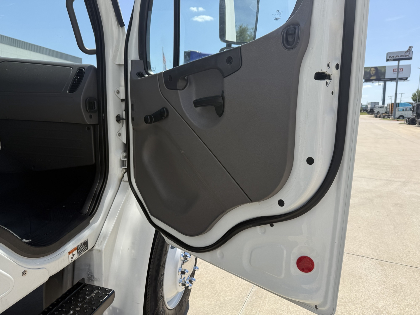 Freightliner M2 cab interior showing open door with beige panel and step, partial view of dashboard and entry area