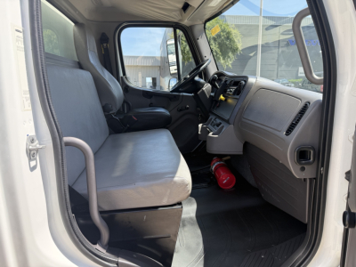 Freightliner M2 cab interior showing front bench seat and dashboard with steering wheel, ignition, and a red fire extinguisher on the floor.