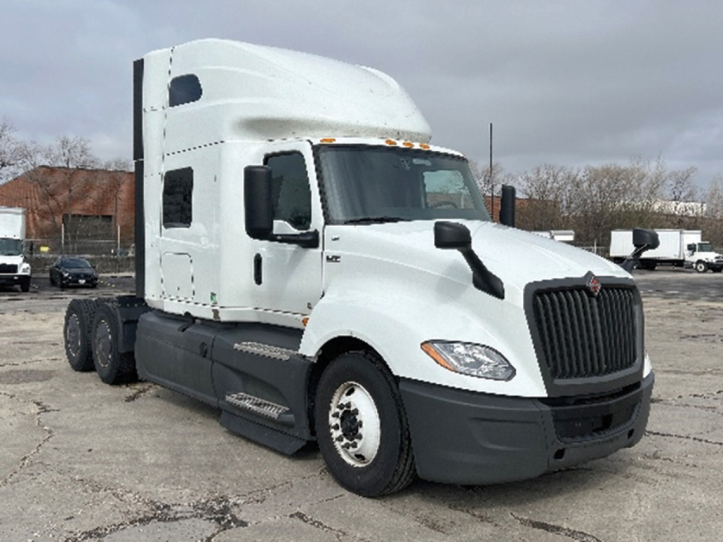 Truck cab chassis showing International LT625 sleeper tractor with white cab, black grille, and dual rear axles on a parking lot.