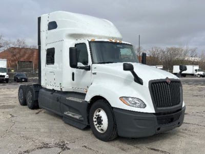 Truck cab chassis showing International LT625 sleeper tractor with white cab, black grille, and dual rear axles on a parking lot.
