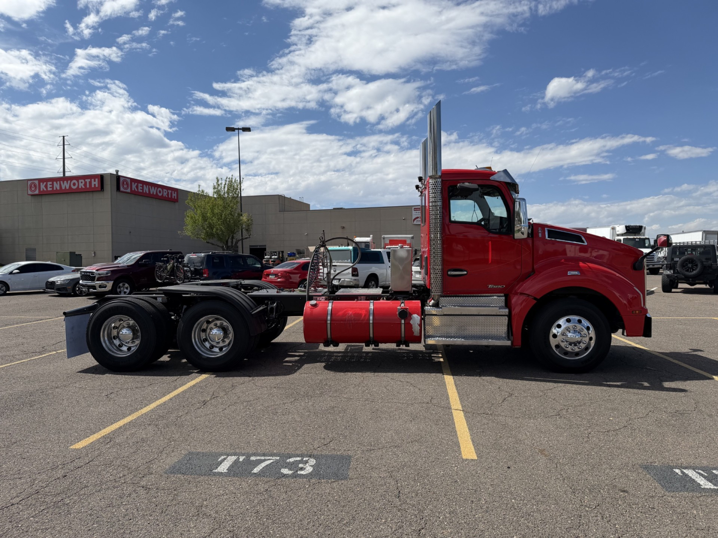 Kenworth T880 conventional daycab semi-truck side view with red cab and black chassis in a parking lot.