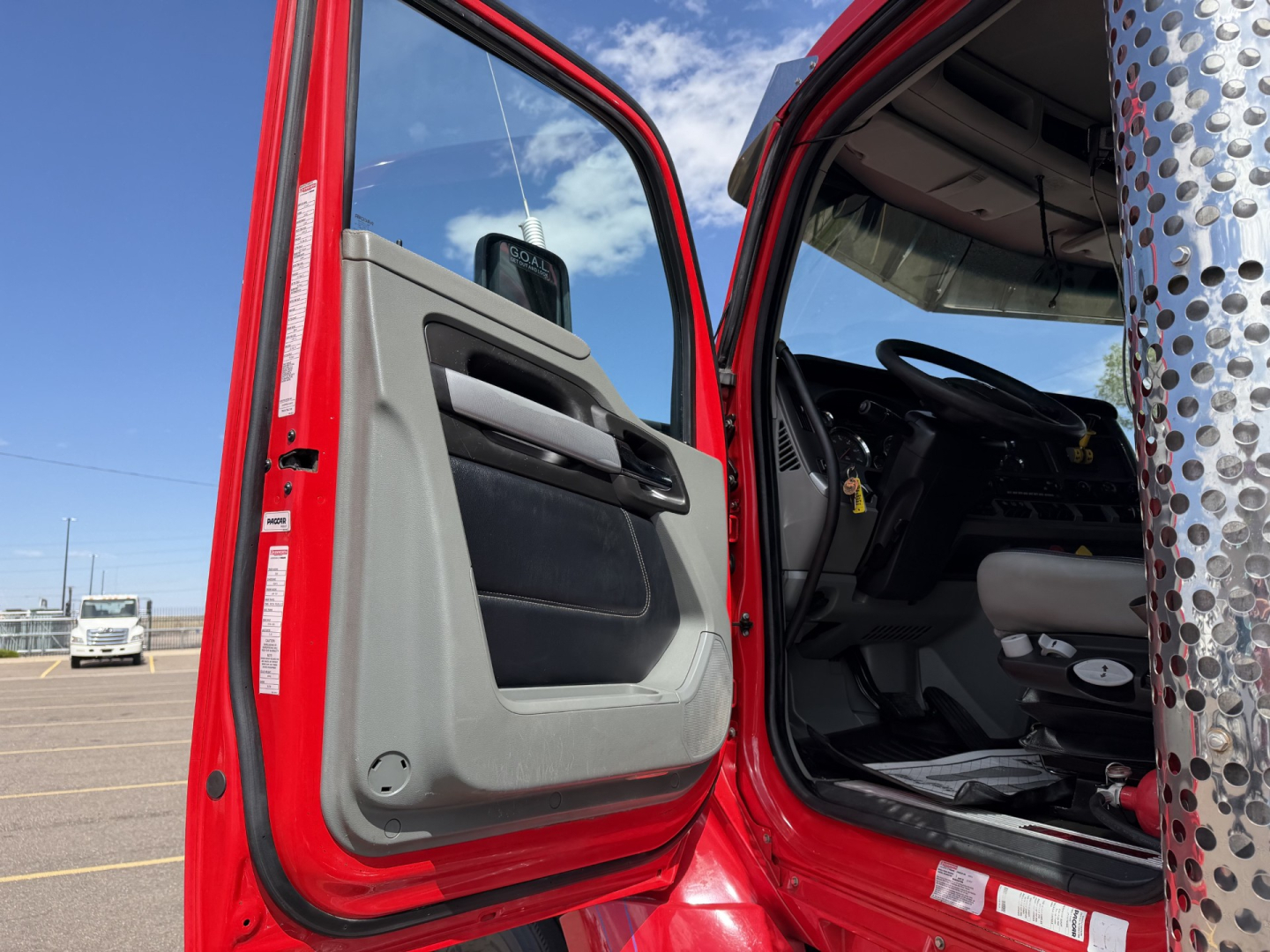 Kenworth T880 cab interior and door area visible from open driver door; red exterior; dashboard and steering wheel seen; partial pillar with perforated metal exhaust stack on side.