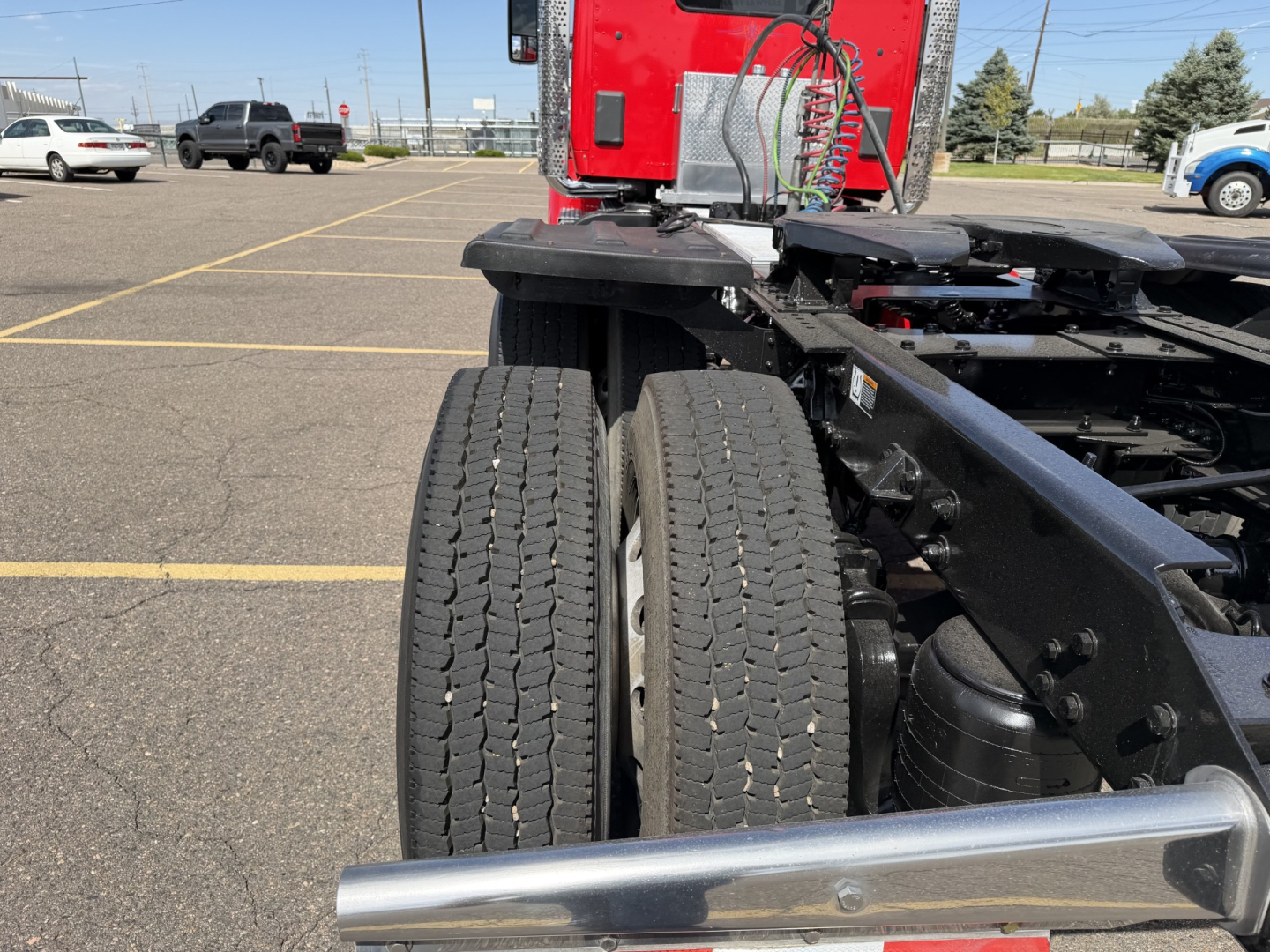 Kenworth T880 rear view showing dual rear axles and chassis with red cab in background.
