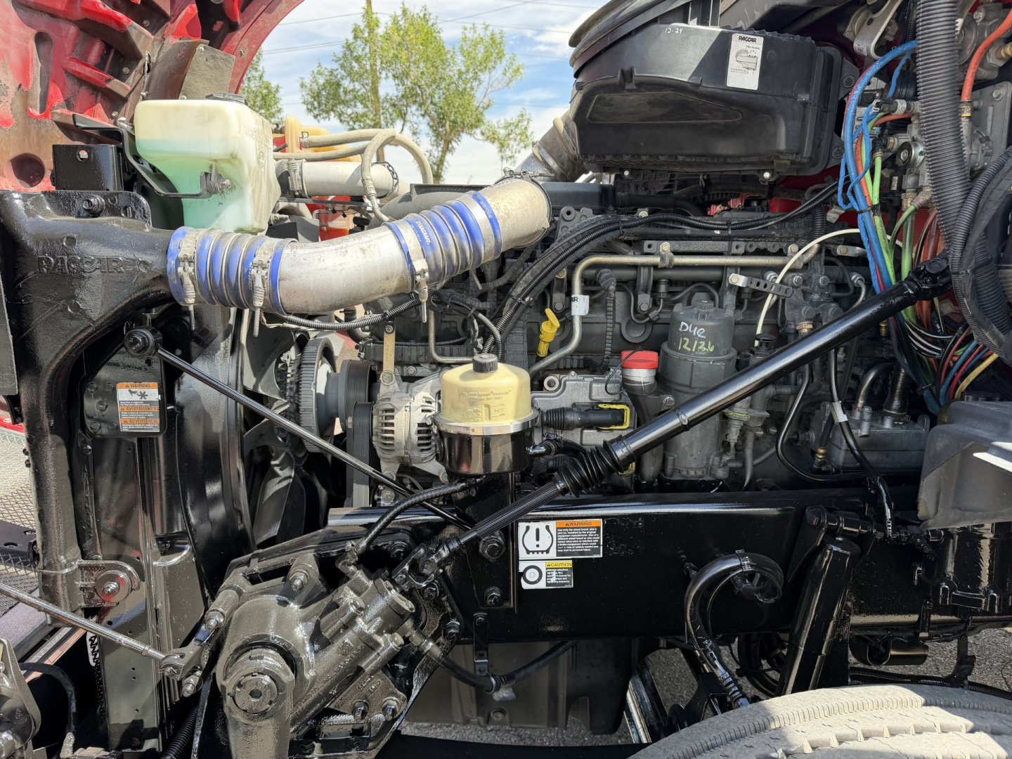 Kenworth T880 engine bay with visible hoses, wiring, and engine components; includes coolant reservoir and various labels.