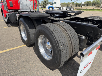 Kenworth T880 rear wheel area showing dual rear axles with tires and chrome wheel covers, trailer connection area, part of red cab visible.