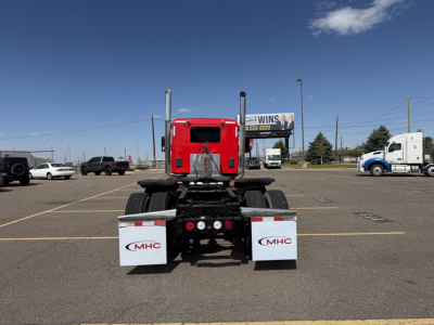 Kenworth T880 rear view showing mud flaps and chassis, red cab, dual rear axles, in a parking lot.