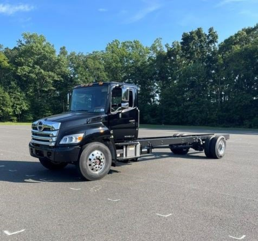 Black Hino L7 cab chassis truck with flatbed, front grille, large tires, side steps, and cab doors visible; engine and branding not legible; clear blue sky.