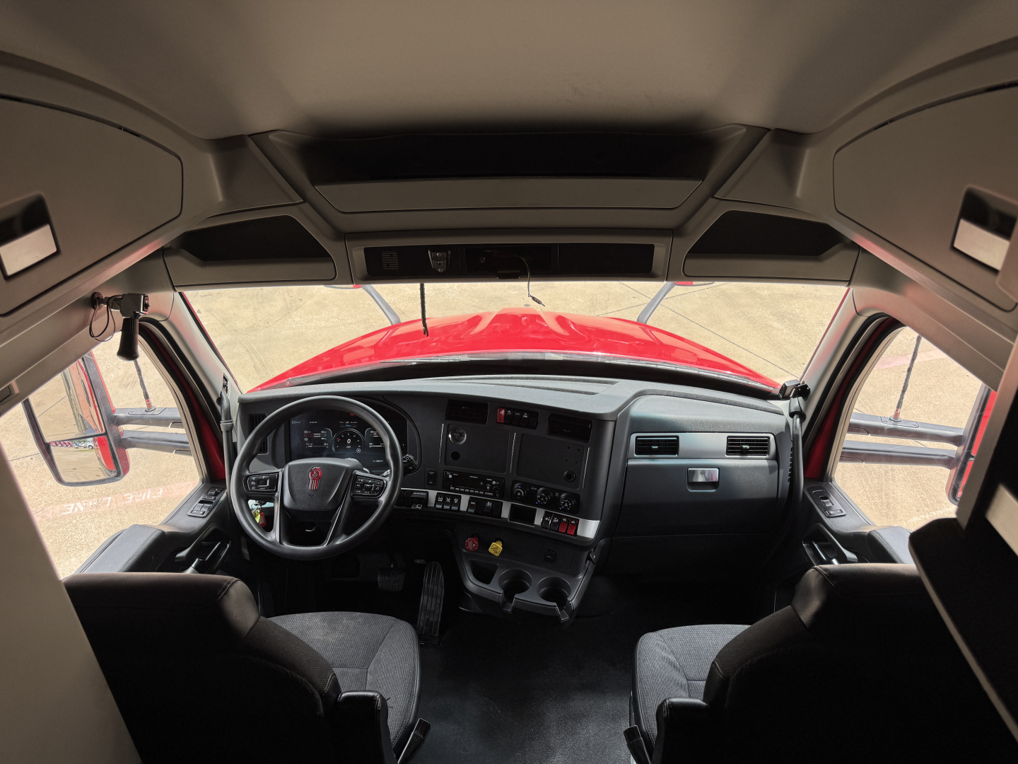 Kenworth T680 cockpit dashboard and steering wheel view from driver seat, with center console, gauges, and windshield.
