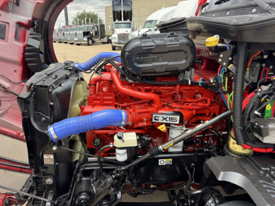 Kenworth T680 engine bay with bright red engine, blue hoses, black air intake cover, and various fluid reservoirs visible.