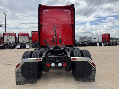 Kenworth T680 tractor rear view showing red cab, dual rear axles, and support mudflaps with diamond-pattern guards.