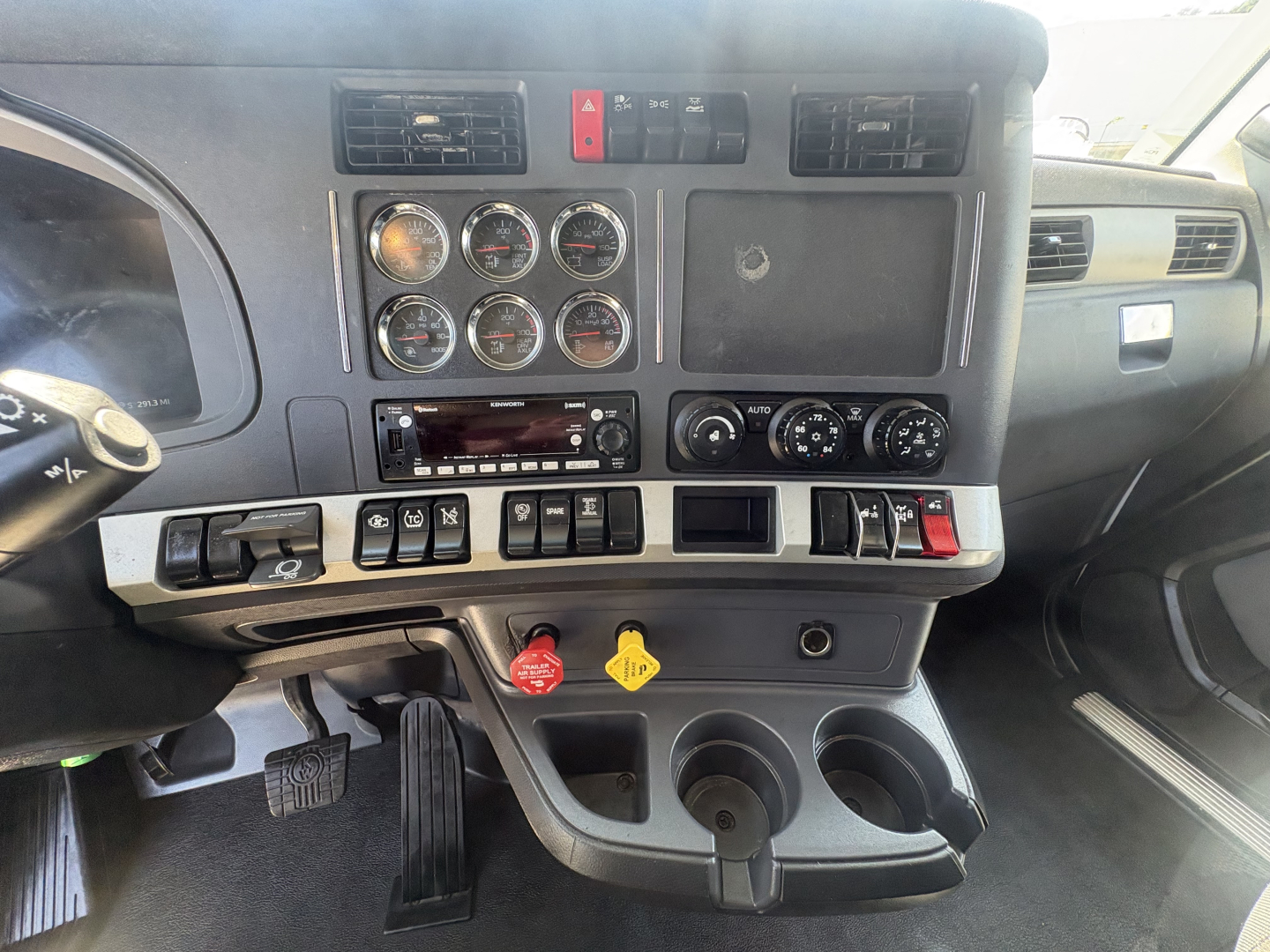 Kenworth T680 dashboard with multiple gauges, switches, and cup holders visible in the cab interior.