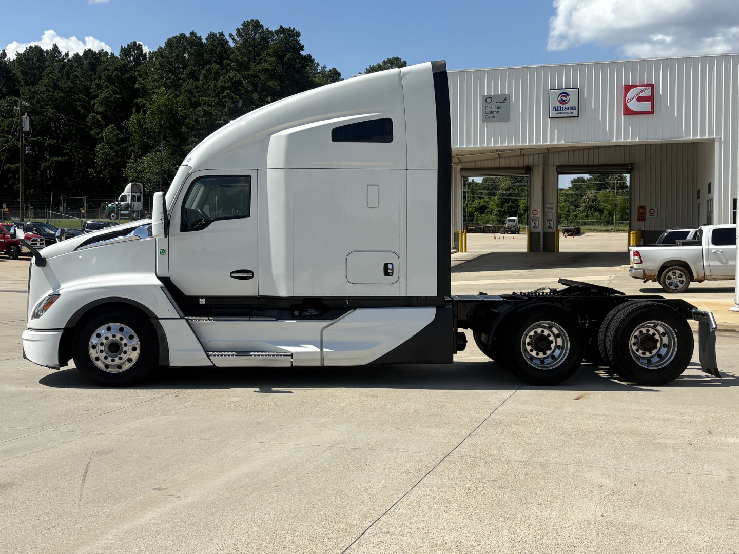 Kenworth T680 tractor-trailer in side profile view with sleeper cab, 6-wheel rear, white color, dealership background