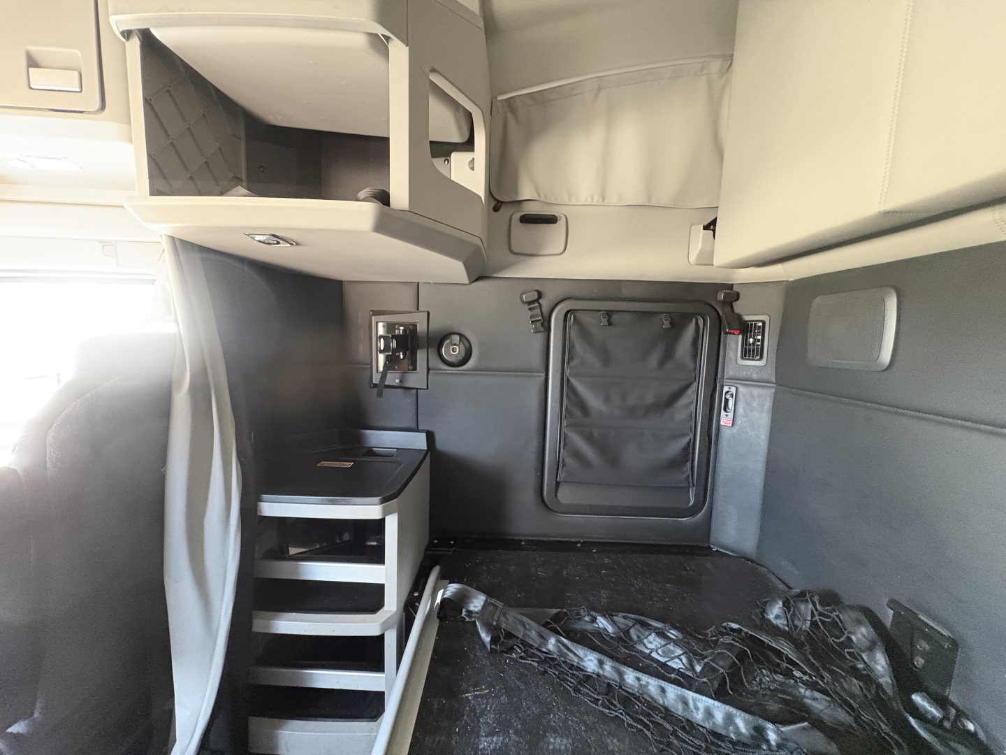 Kenworth T680 sleeper cab interior showing storage compartments, overhead shelf, and side entry door; cabin area with cabinet, steps, and seating visible.
