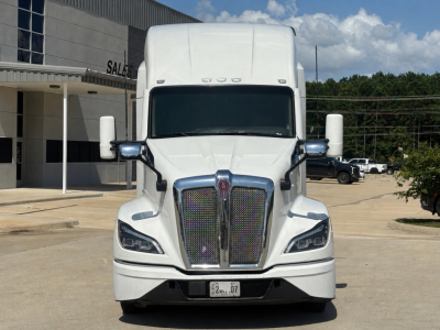 Kenworth T680 front view showing large grille with chrome surround, dual wiper-less windshield, rectangular headlights, white cab, side mirrors, and bumper with license plate area.