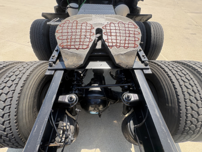 Rear view of a Kenworth truck chassis with dual rear axles and fifth-wheel area; visible components include leaf springs, driveline, and suspension. No legible brand text visible on image.