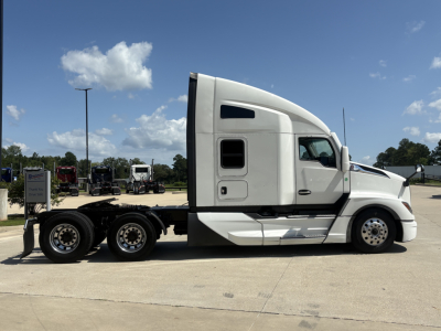 Truck side view of a white 2022 Kenworth T680 tractor with sleeper cab, flatbed trailer chassis, and dual rear axles.