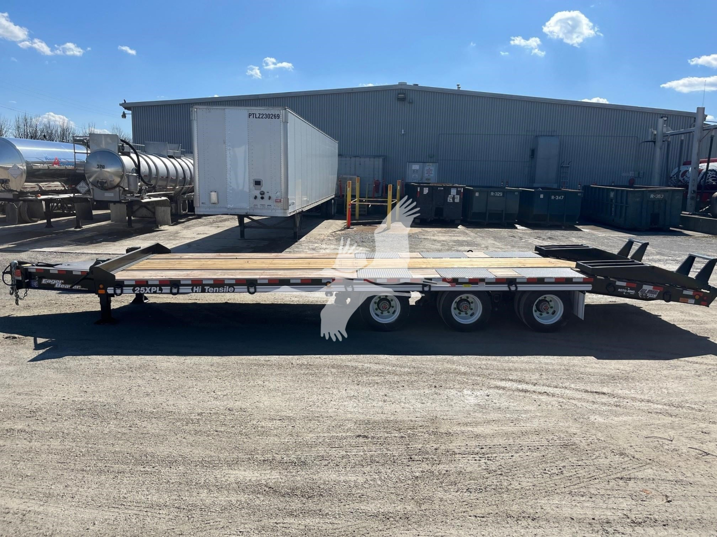 Trailer showing a flatbed trailer with triple axles and a refrigerated unit on the hitch, in an industrial yard.