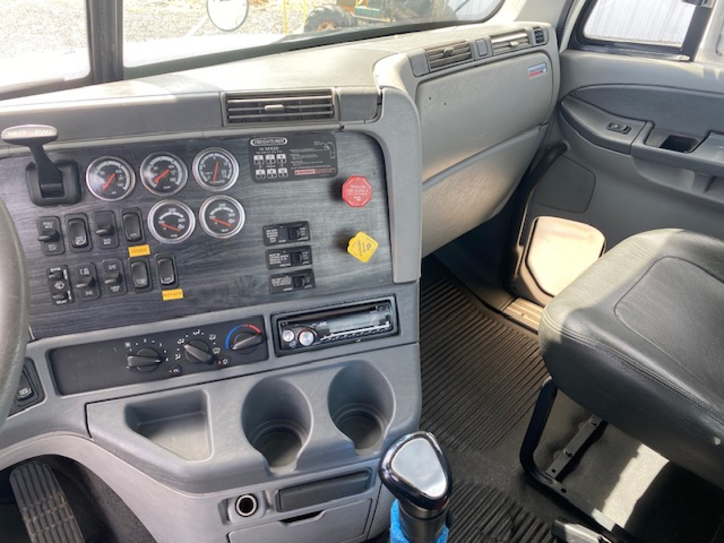 Truck cab dashboard panel with multiple gauges, switches, and controls; gear shifter, cup holders, and empty storage compartments visible.