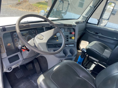 Truck cab interior showing steering wheel, dashboard, gauges, and driver seat in a Freightliner Columbia CL120ST.