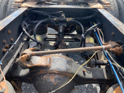 Truck rear undercarriage showing differential, drive axles, and suspension with rusted components and wiring harnesses in view.