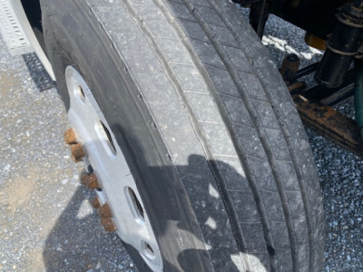 Truck wheel close-up showing high-mileage tire tread and steel wheel, with partial chassis and suspension components visible.