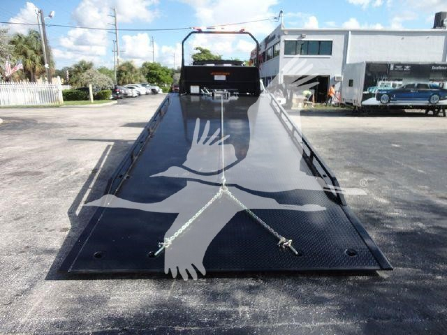 Black metal rollback ramp with two white hands graphic, steel surface with tie-down points, and a rear access area on a truck dealership lot.