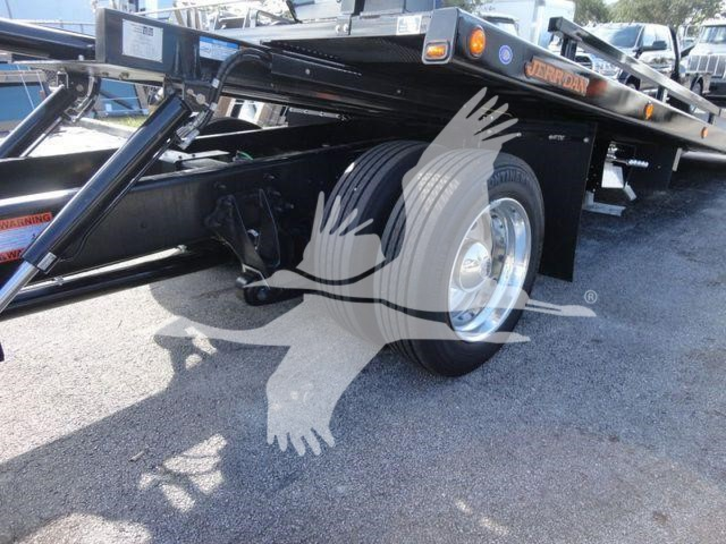 Side view of a flatbed rollback truck chassis with dual rear wheels and a black steel frame. Visible text on a sticker near the hitch reads 'Jerr-Dan' and there are warning labels on the side.