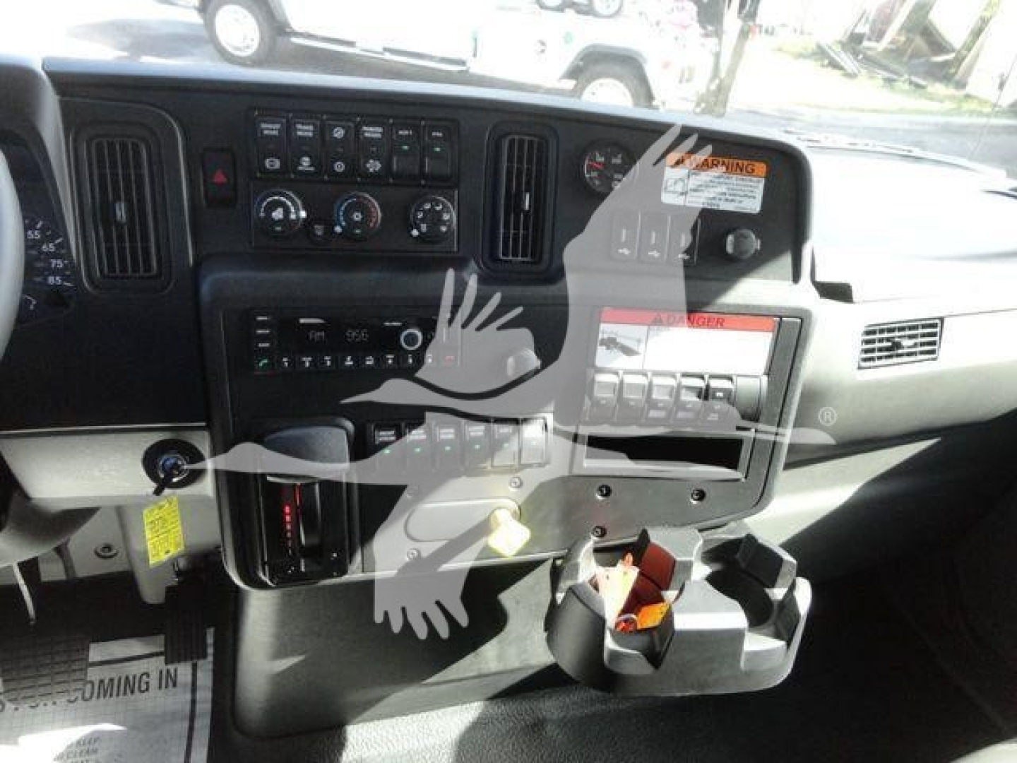 Dashboard of a truck cab showing control panel, gauges, vents, and a cup holder. Visible text includes warning label, push buttons, and dials.