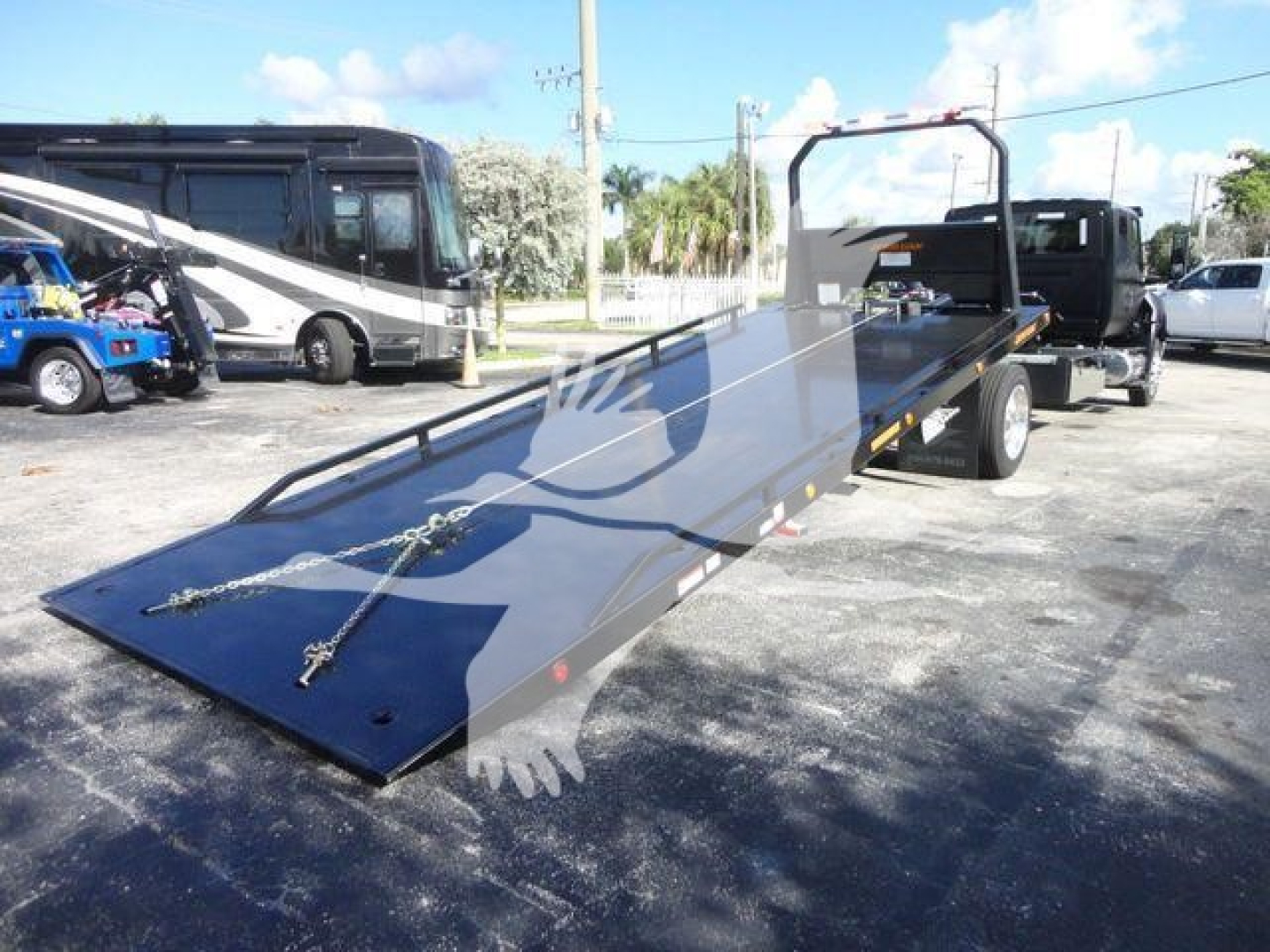 Flatbed tow truck with rear ramp extended, MV International truck in background.