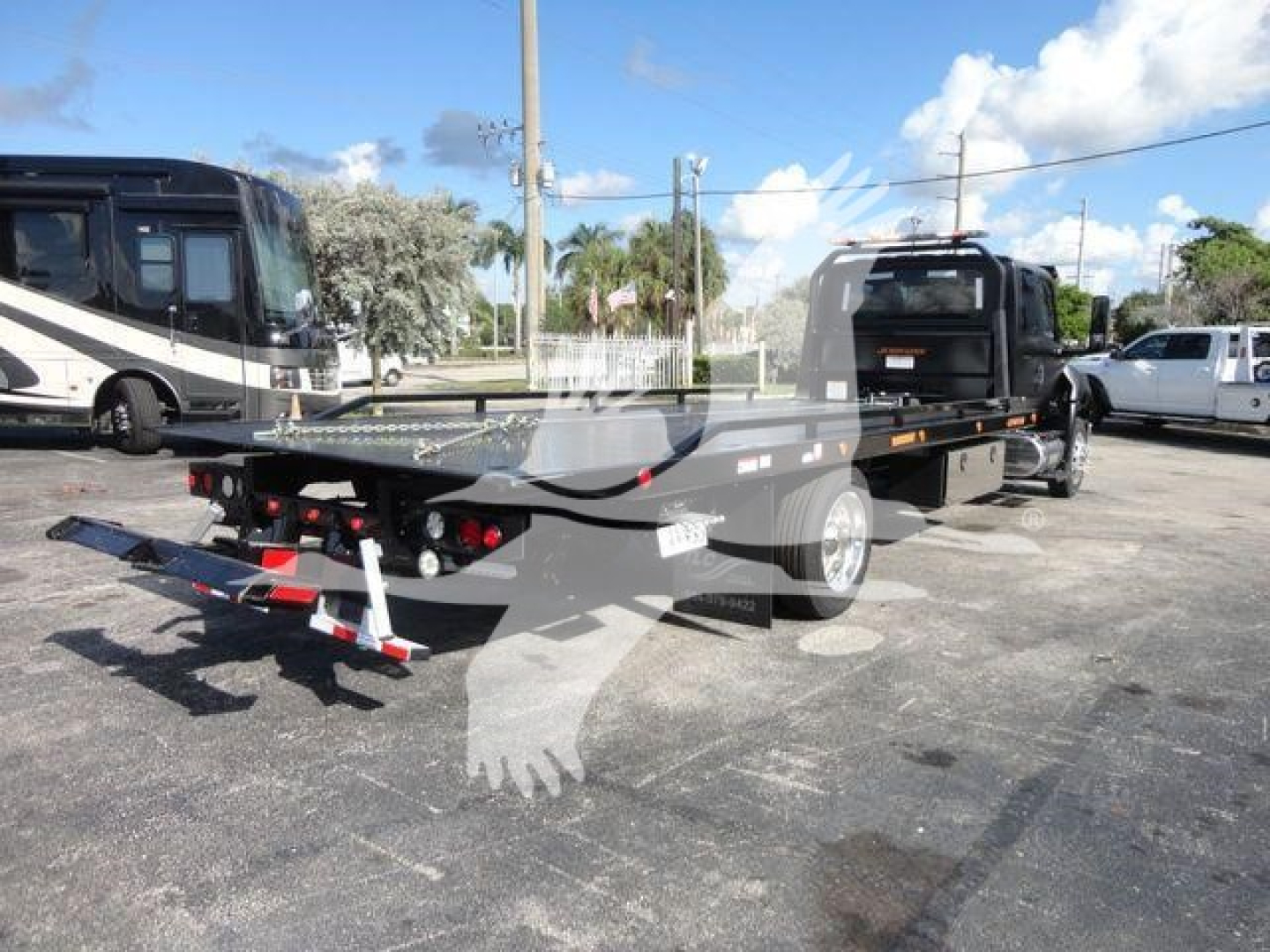 Flatbed tow truck chassis with rear pneumatic ramp and hitch, side profile, black paint, trailer bed with stake pockets.