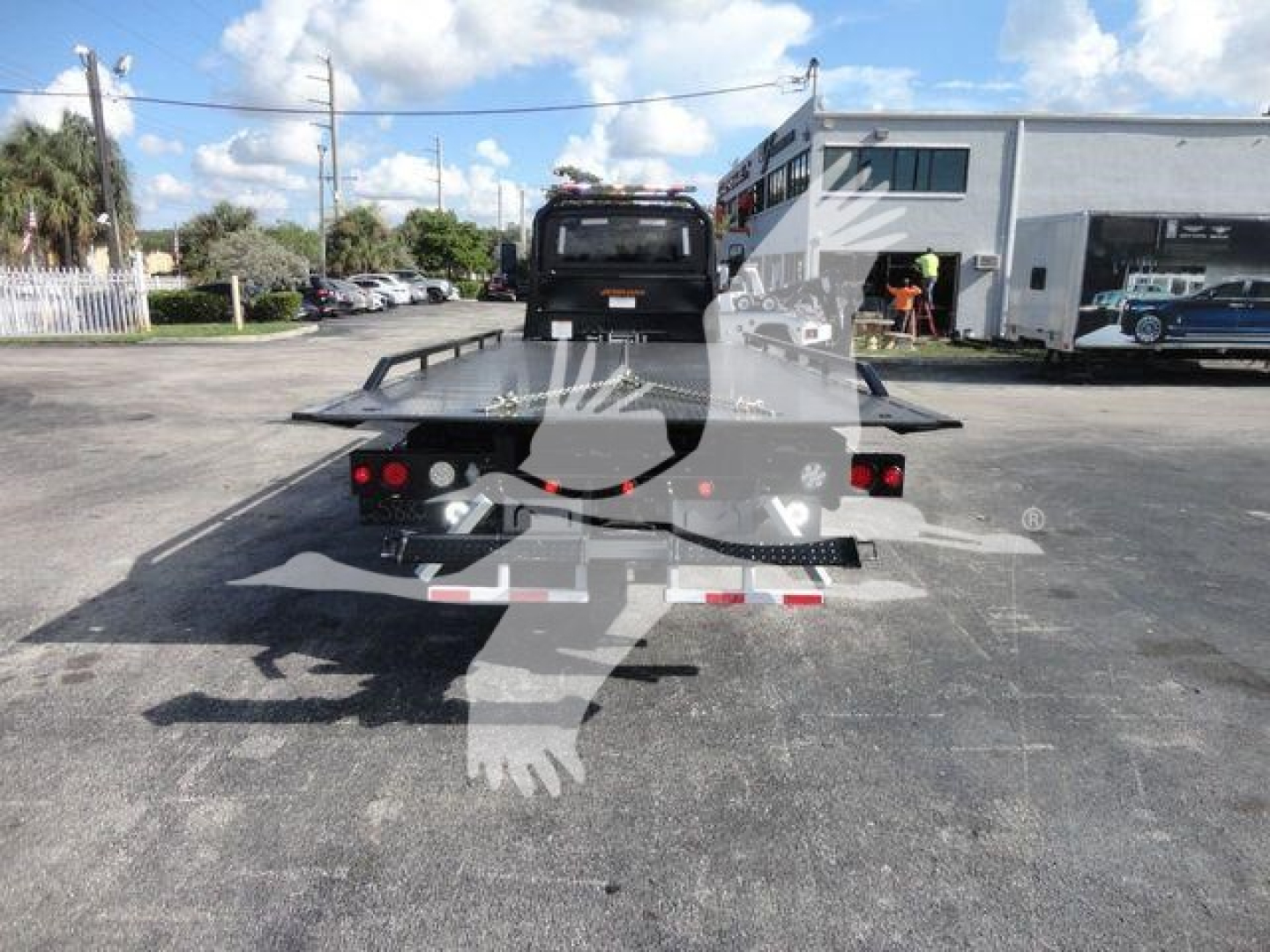 Flatbed tow truck platform at rear with ramps, International MV chassis visible in a dealership lot.