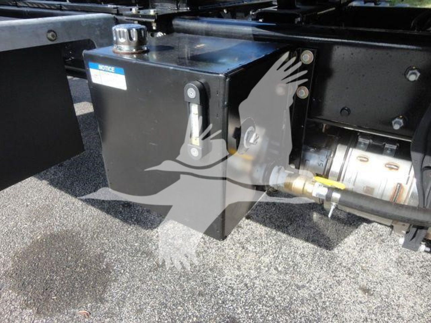 Truck hitch area showing a black metal box with a cap and a hose fitting, mounted on the frame of a heavy-duty International MV rollback truck.