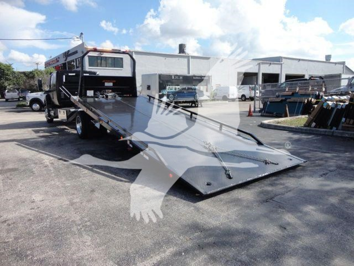 Truck with lowered flatbed ramp in an outdoor lot; International MV cab visible in background.