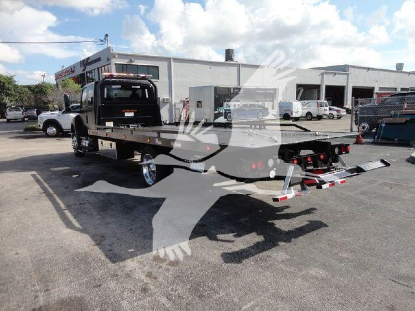 Truck bed with rollback equipment on a black International MV chassis, flatbed and winch, visible in a dealership lot.