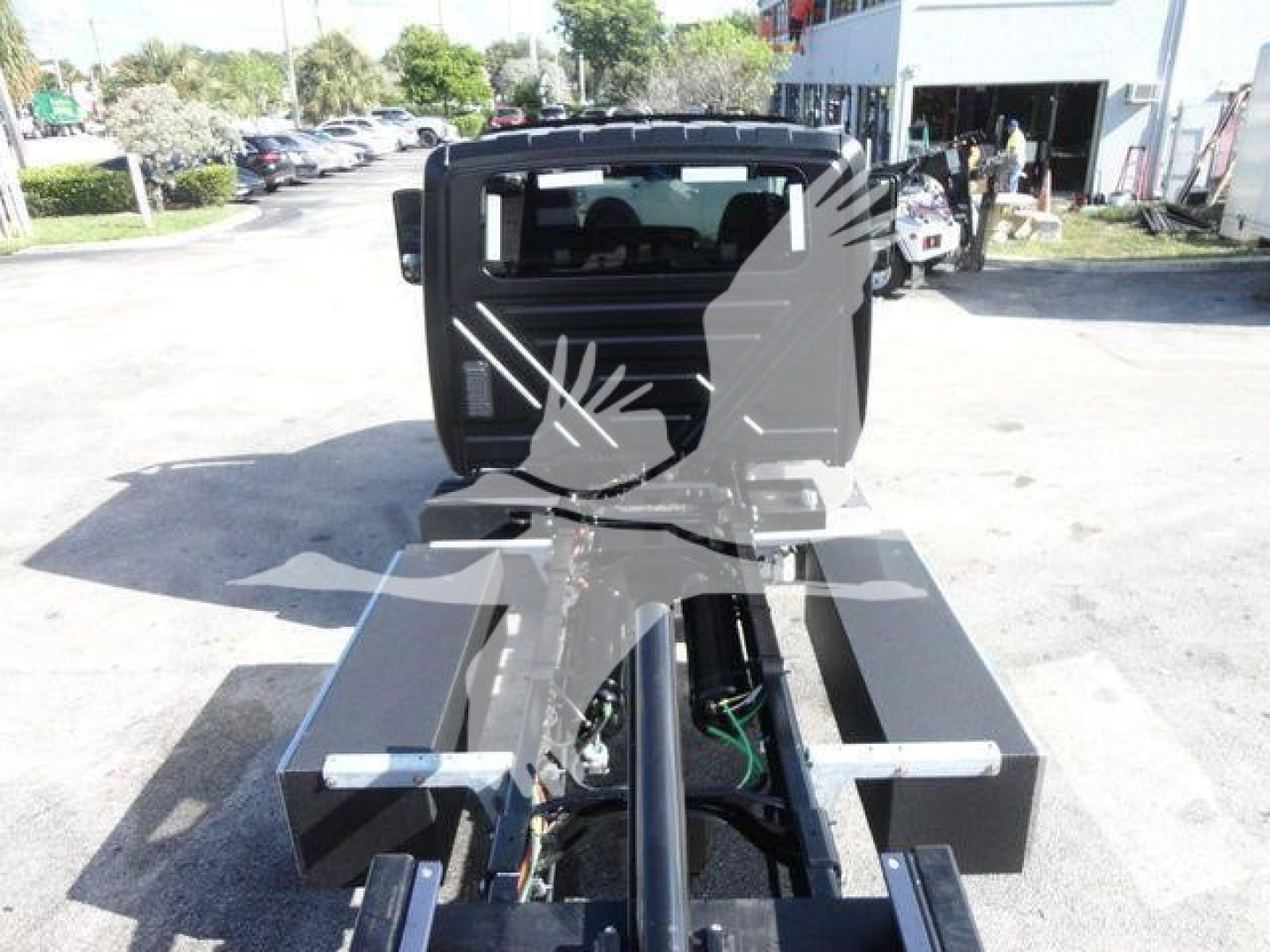 Truck chassis with cab in background showing frame and hydraulic components for rollback truck.