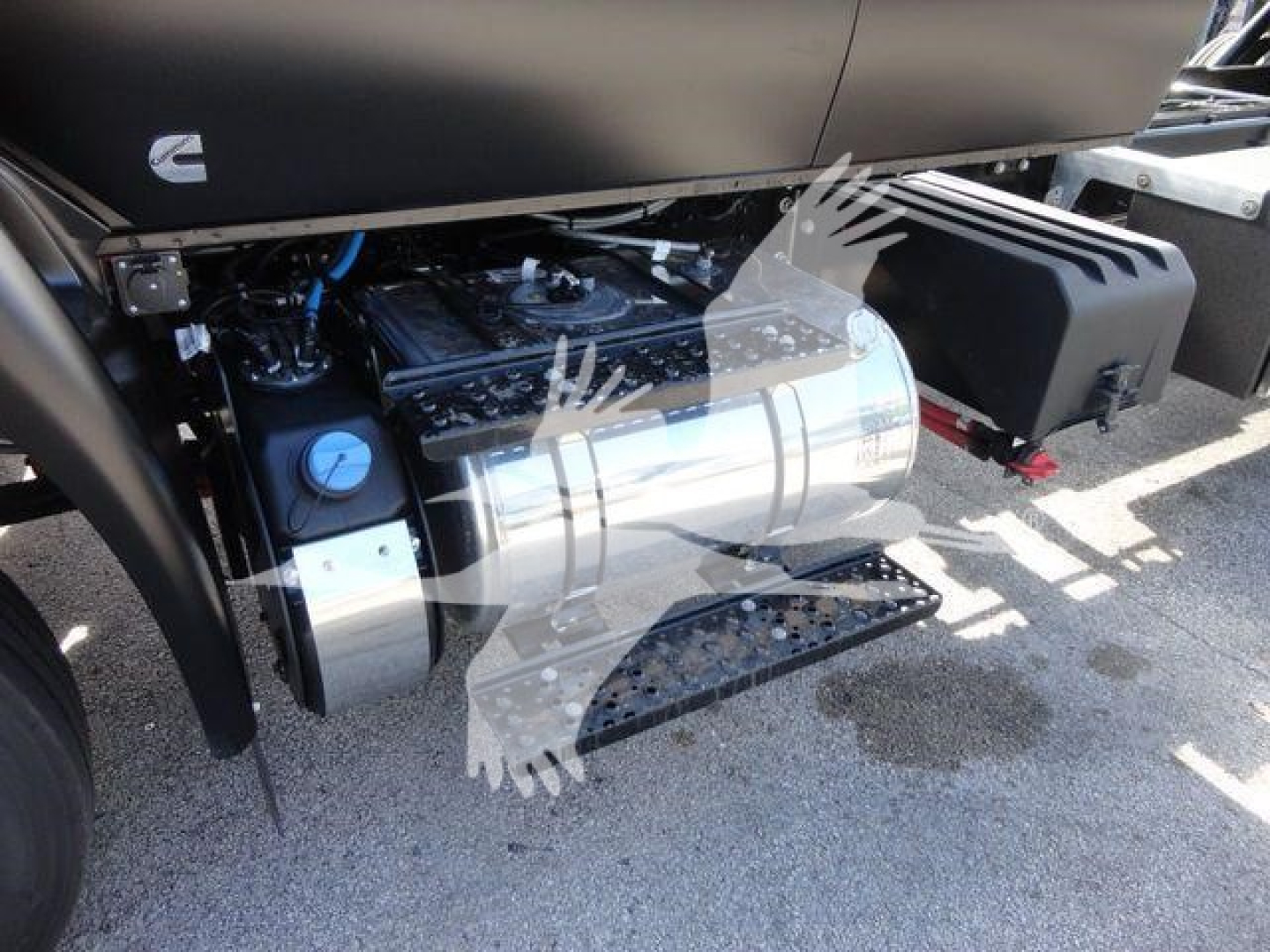 Truck engine bay showing cylindrical fuel tank and metallic components on left, side steps and black plastic fairing on right.