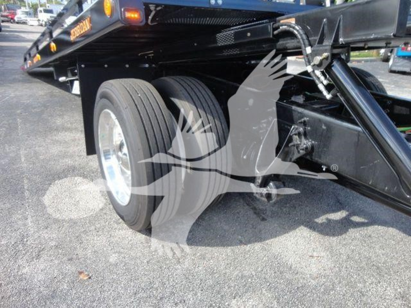 Truck towing equipment with dual rear wheels and hydraulic tow mechanism seen from side; flatbed with black frame and metallic components.