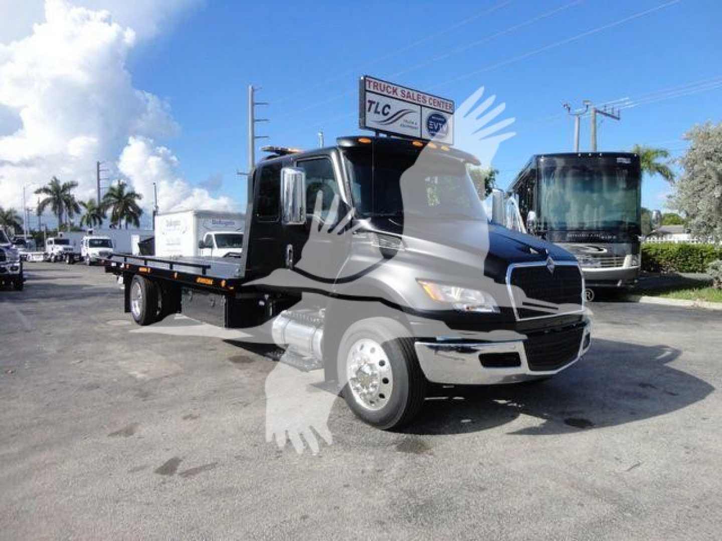 Truck: 2027 International MV rollback truck in service-ready condition with a flatbed chassis and twin-axle rear, parked in lot with other trucks.
