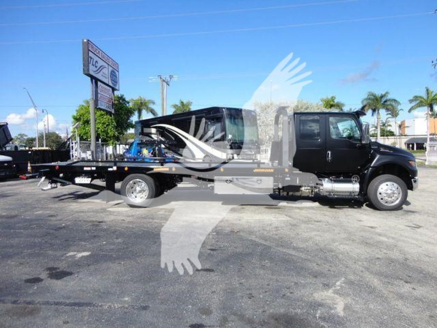 Truck cab and flatbed equipment hauler side view showing International MV with long wheelbase and dual rear axles, clear weather, dealership lot.