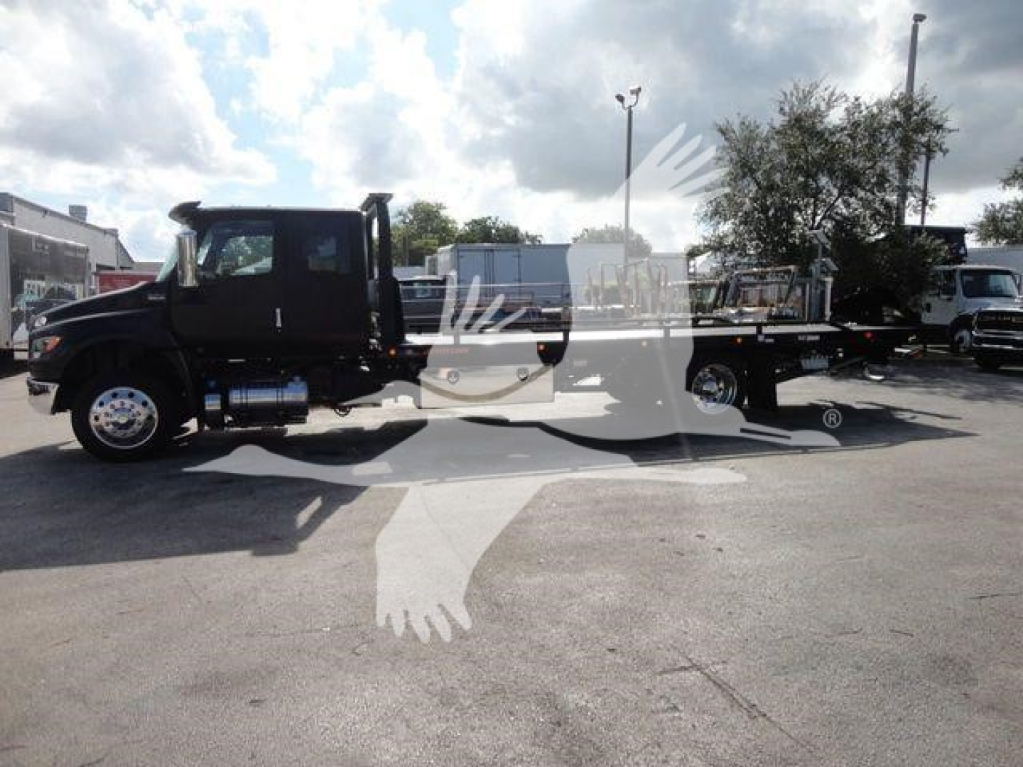 Truck cab and long flatbed rollback w/ dual rear axles, black color, side view showing International MV label? visible text not clear.