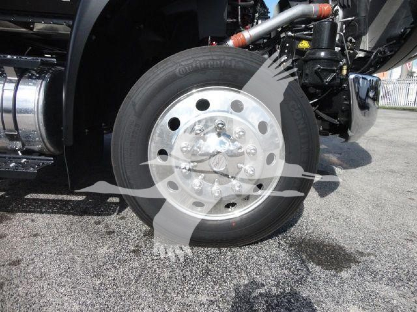 Truck wheel and front suspension visible with polished aluminum hubcap and tire; part of International MV rollback configuration.
