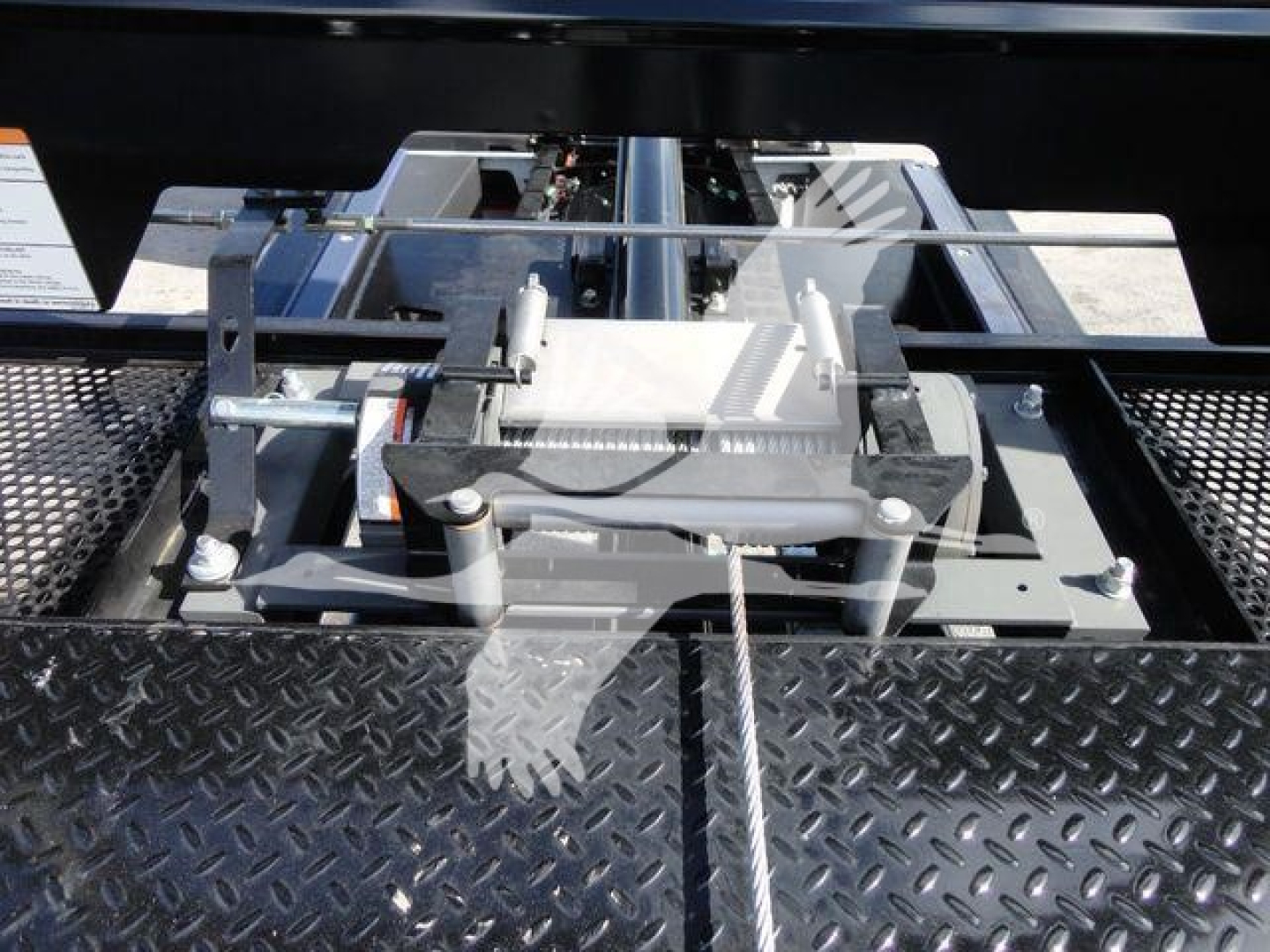 Truck equipment in a rollback bed showing a hydraulic winch mechanism and steel anchor plate with cables and controls.
