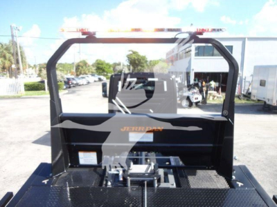 Truck rollback equipment frame with top light bar and platform; visible branding shows Jerr-Dan on the side; outdoor lot with other vehicles in background.