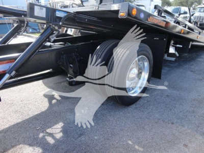 Side view of a flatbed rollback truck chassis with dual rear wheels and a black steel frame. Visible text on a sticker near the hitch reads 'Jerr-Dan' and there are warning labels on the side.