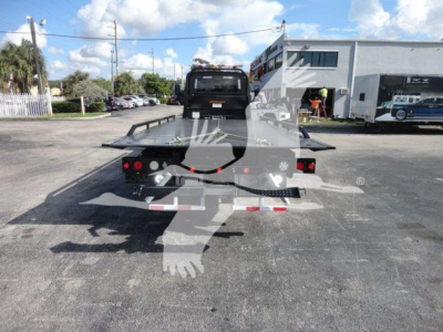 Flatbed tow truck platform at rear with ramps, International MV chassis visible in a dealership lot.